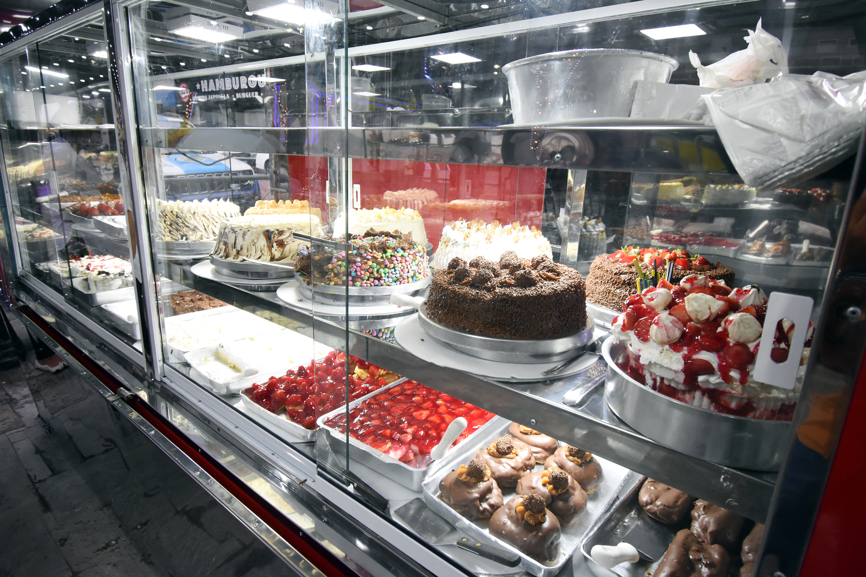Vitrine de vidro de um trailer com bolos confeitados, tortas de morango e doces de chocolate.