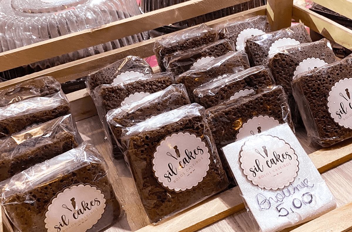 Fatias de bolo e brownie embaladas com etiquetas expostas em caixotes de madeira.