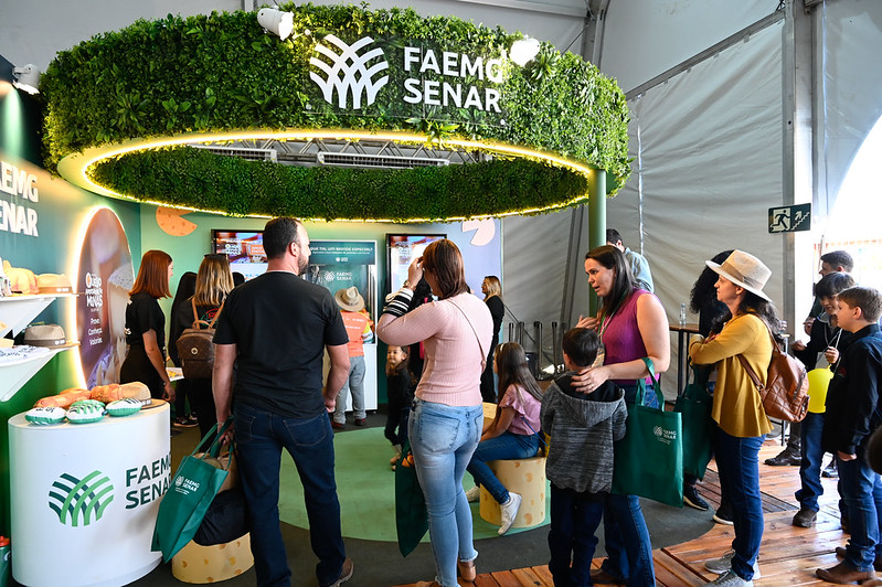 Visitantes, incluindo crianças, em volta do estande FAEMG SENAR sob a tenda do festival.